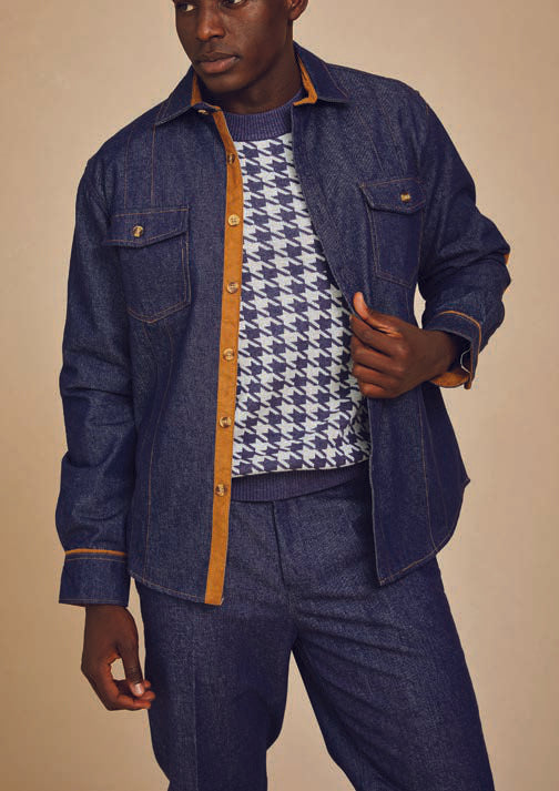 A person is dressed in the Inserch Denim Two-Pocket Shirt SE003A-10 in Denim Blue, featuring faux suede trim, layered over a houndstooth patterned sweater and paired with matching denim pants. The outfit is accented by novelty marled buttons, all set against a beige background.