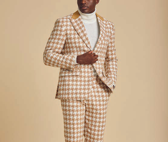 Dressed in the Inserch Wool Blend Houndstooth Check Peak Lapel Suit BL264-09 Khaki, a person pairs it with a white turtleneck and white sneakers, standing against a beige background.