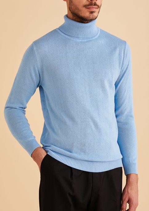 A man wearing the Inserch Cotton Blend Slim Fit Turtleneck Sweater in Blue Mist and black pants stands against a beige background.