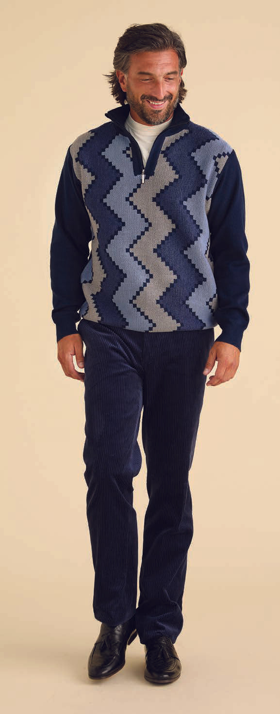 A man dressed in navy Inserch Premium Cotton Flat Front Corduroy Pants P267-11 stands against a beige background, wearing a sweater with a zigzag pattern.