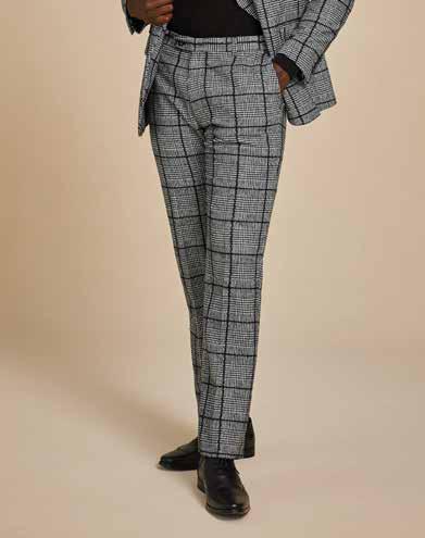 A person dressed in Inserch Glenn Check Pants P504-41 in black and white, paired with a modern fit gray plaid suit crafted from a wool-blend glenn check fabric and black shoes, standing against a beige background.