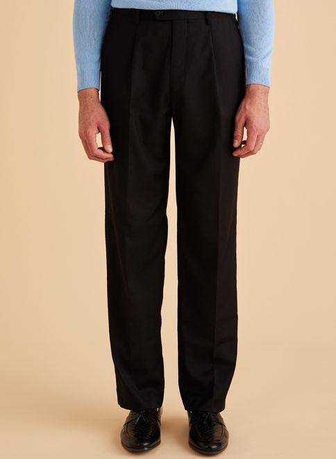 A person wearing Inserch One Pleat Pants P0599S-00001 in black, a light blue sweater, and black shoes stands against a beige background.