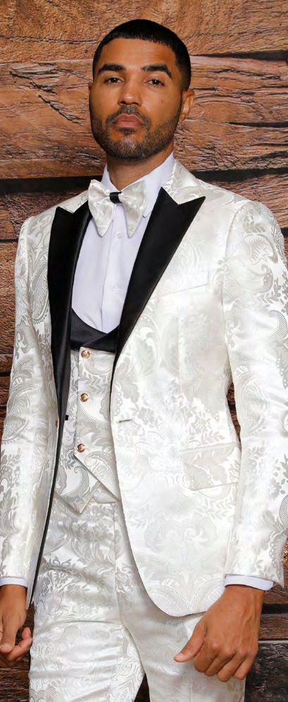 A man in an INSOMNIA ARMANI Slim Fit Cream Black Fancy Woven Suit, featuring a black lapel and complemented by a bow tie, stands against a wooden background.