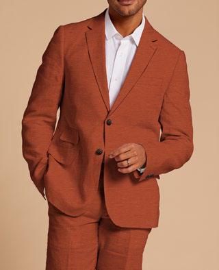 A person dressed in an Inserch Slim Linen Suit SU880-00109 Burnt Orange paired with a white shirt stands against a beige background, highlighting the elegance of this premium ensemble from Inserch.