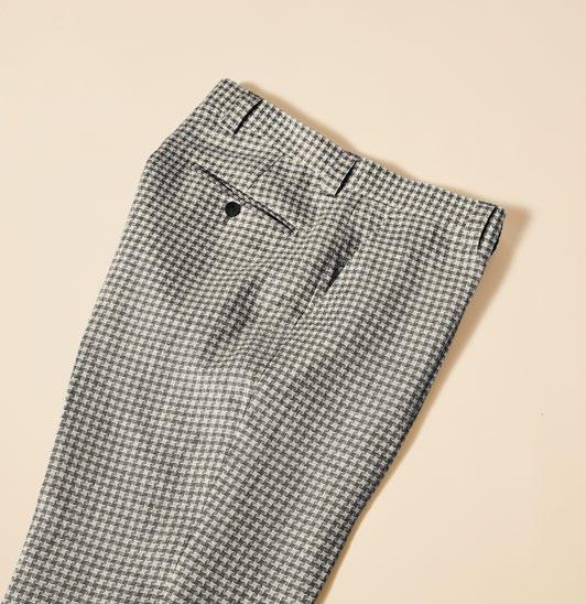 A person wearing Inserch Linen Houndstooth Pants in black and white, paired with brown shoes, stands against a beige background.