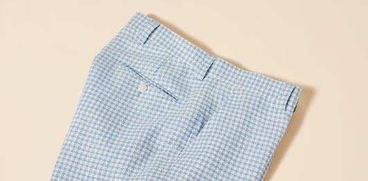 A person dressed in Inserch Linen Houndstooth Pants P269-00014 in light blue and brown dress shoes poses against a beige background, showcasing subtle sophistication with a touch of premium linen texture.