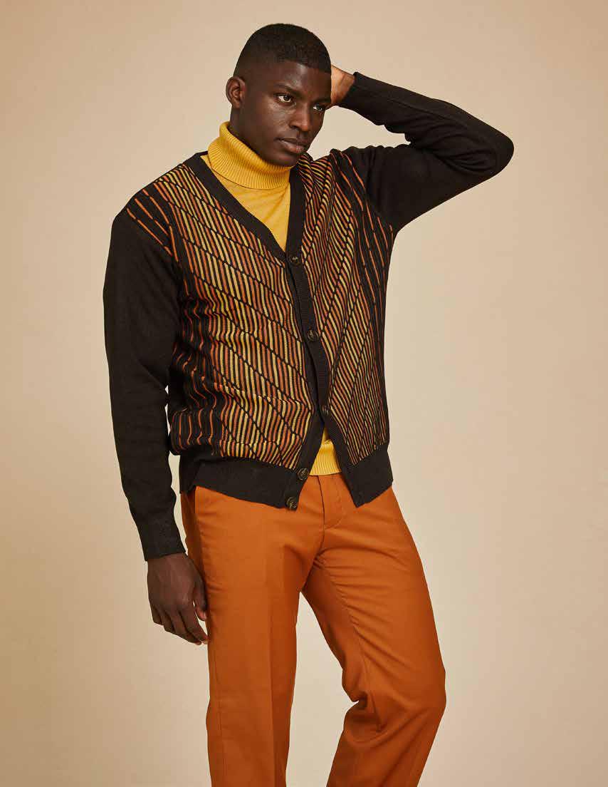 A man wearing the Inserch Intarsia Panel Cardigan SW904-24 Chocolate, which features a geometric intarsia pattern with multicolored diagonal stripes, paired with a mustard turtleneck and jeans.