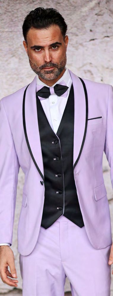 A man confidently poses against a light background in the INSOMNIA SUNSET 3PC Slim Fit Lavender Tuxedo Suit by Insomnia, featuring black trim, a crisp white shirt, and a black bow tie, with his stylish look enhanced by a sleek reversible vest.