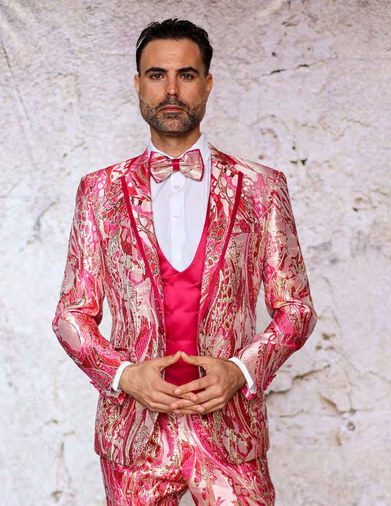 A person wearing the INSOMNIA SANTO 3PC Tailored Fit Fuchsia Suit by Insomnia, along with a matching vest and bow tie, stands against a textured white background.