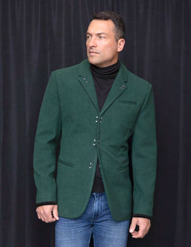 A person stands in front of a black curtain, showcasing a tailored fit with the INSOMNIA MZS-502 Hunter Fancy Sport Coat, complemented by a black turtleneck and blue jeans.