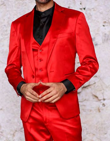 Dressed in the INSOMNIA CLASSICO 3PC Tailored Fit Satin Spandex Red Suit by Insomnia, which includes a vibrant red ensemble complemented by a sleek black shirt, the person poses confidently against a textured light background.