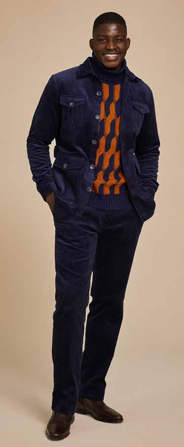 Wearing the Inserch 4-Pocket Cord Suit BL267-11 in a modern fit, complemented by an orange and blue patterned sweater, a man stands confidently against a beige background. The navy blue corduroy jacket and pants from Inserch add texture to his ensemble, highlighted by an adjustable back tab for tailored comfort.