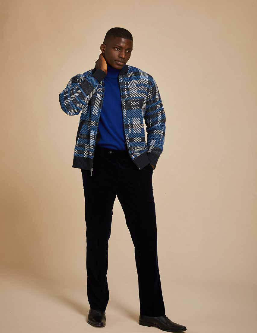 A man wearing the Inserch Geometric Full Zip Baseball Knit Jacket in navy, crafted by Inserch, stands against a beige background. He has styled it with a white shirt, gray jeans, and white sneakers. His hands rest calmly by his sides.