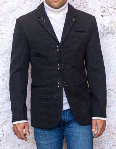 A man stands against a light textured background, wearing the INSOMNIA MZW-502 Tailored Fit Black Fancy Sport Coat by Insomnia, paired with a white turtleneck and blue jeans.