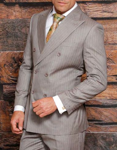 A person in a stylish INSOMNIA ATLAS 2PC Double Breasted Modern Fit Tan Suit from Insomnia, complemented by a patterned tie, stands against a wooden background.