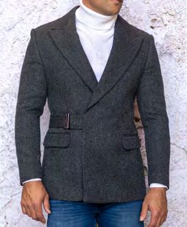 A person wearing the INSOMNIA MZS-567 Tailored Fit Charcoal Fancy Sport Coat over a white turtleneck sweater and blue jeans stands against a textured wall.