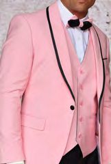 A man wears the INSOMNIA SUNSET 3PC Slim Fit Pink Black Tuxedo Suit by Insomnia, featuring a pink tuxedo with black trim and a matching reversible vest. His outfit is finished off with a crisp white shirt and a coordinated pink and black bow tie.