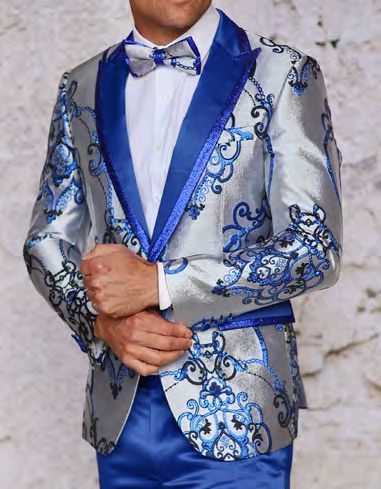 Dressed in the INSOMNIA MZS-538 Tailored Fit Royal Woven Sport Coat by Insomnia, a person stands against a light background. The silver and blue ornate suit they wear is complemented perfectly by a matching bow tie, adding just the right touch of elegance to their sophisticated look.