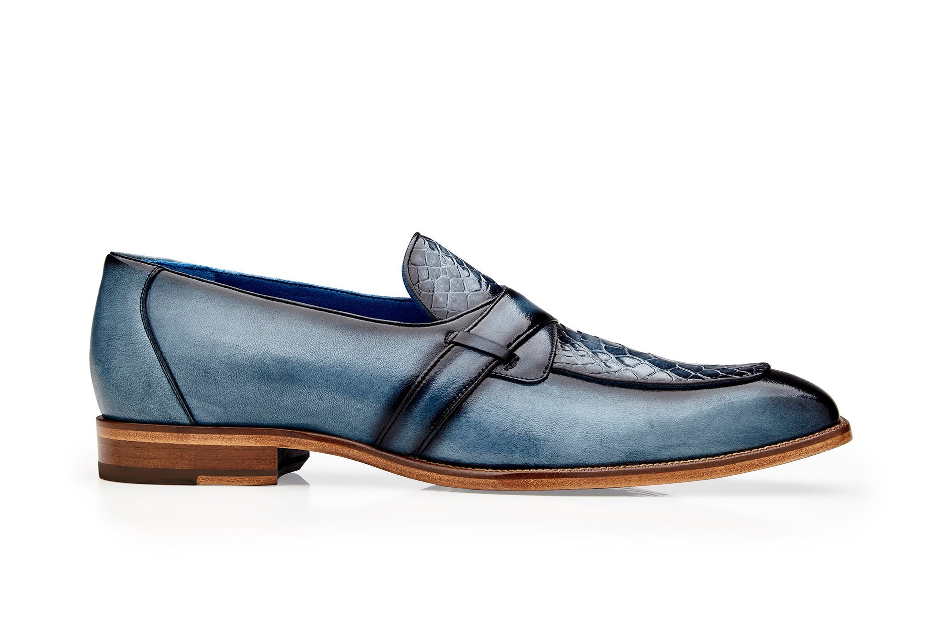 Introducing the Belvedere - Tornado, a stylish slip-on loafer crafted from Genuine American Alligator and Italian Calf leather in an antique blue jean color. This dress shoe features a textured upper and a wooden sole, beautifully showcased from the side.