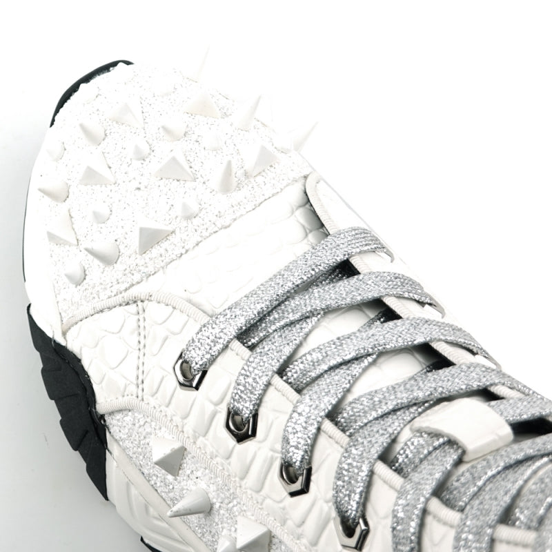 Introducing the FI-2405 White Spikes High Top Sneakers Encore by Fiesso, a striking fashion-forward design from Fiesso. These sneakers boast a textured white exterior accented with shimmering silver laces and adorned with numerous glittering spikes across the sides and front. The look is completed with a bold chunky black-and-white sole that instantly catches the eye.