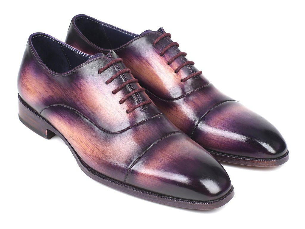 A pair of Paul Parkman Captoe Oxfords, model 1744-PRP, featuring a glossy multicolored finish that transitions from purple to pink on hand-painted leather, are laced up with one shoe slightly positioned atop the other.