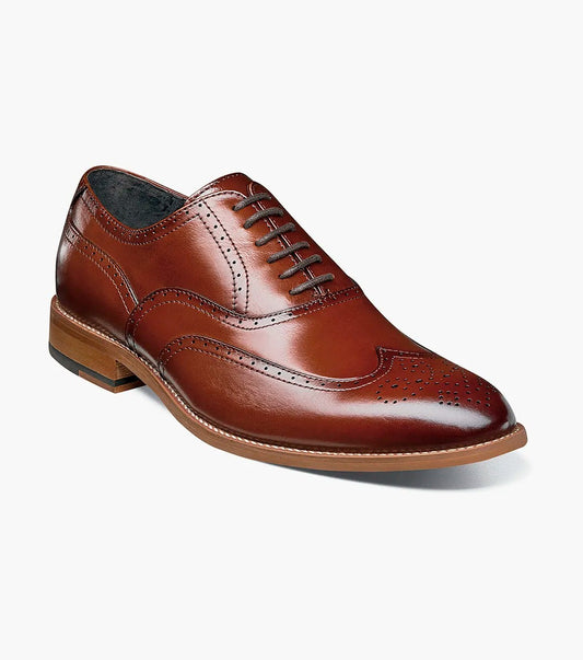 The Stacy Adams DUNBAR Wingtip Oxford shoe, model number 25064-221 in Cognac, showcases a leather upper with intricate stitching and perforations. This elegant design is completed with a low wooden heel, creating timeless sophistication against a white background.