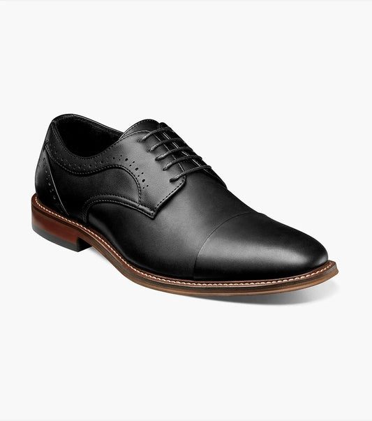 The STACY ADAMS MADDOX Cap Toe Oxford, in black and product number 25488-001, is a leather dress shoe with laces. It boasts a classic design with decorative perforations and is crafted from burnished leather for a sleek finish.