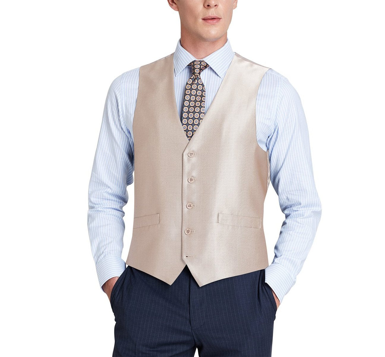 A man dressed in the Renoir Alessandro Vitello Beige Formal Regular Fit Suit Vest, also known as the Sharkskin Waistcoat 207-3, paired with a blue shirt and patterned tie, stands with hands in pockets, exuding sophistication. The beige polyester viscose fabric enhances the elegance of his ensemble.