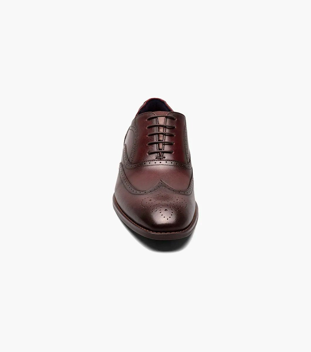 The Stacy Adams KAINE Wingtip Oxford in Burgundy, model number 25569-601, showcases a leather upper with decorative perforations and a classic wingtip design. This brogue dress shoe features a low heel and is photographed on a white background, highlighting its elegance and anatomical arch support for added comfort.