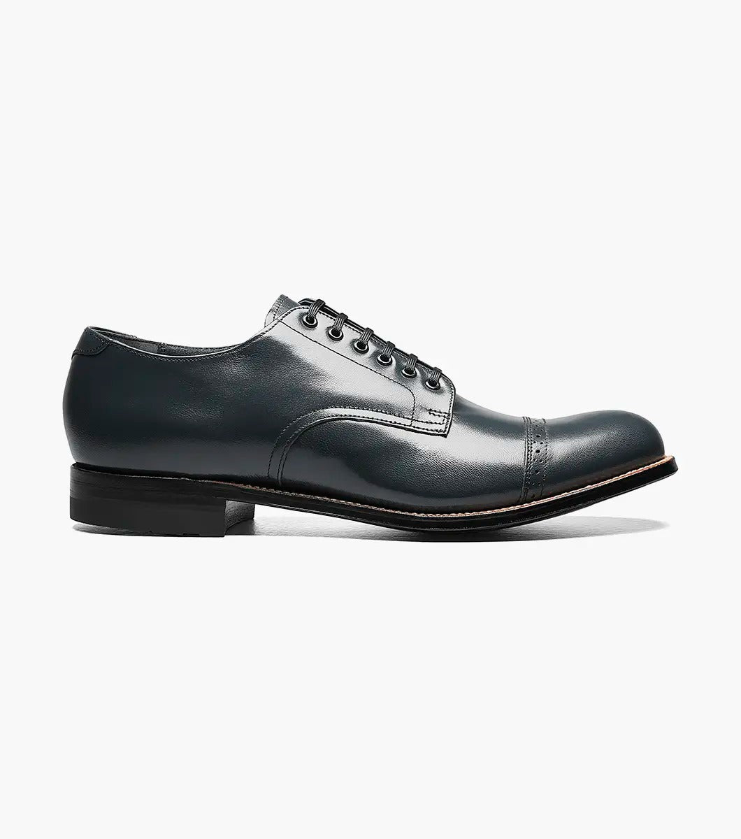 Explore the sophistication of the Stacy Adams MADISON Cap Toe Oxford in navy kidskin leather. This design includes closed lacing, a round toe, and decorative perforations. A cap toe and stacked heel complete the look against a pristine white background.