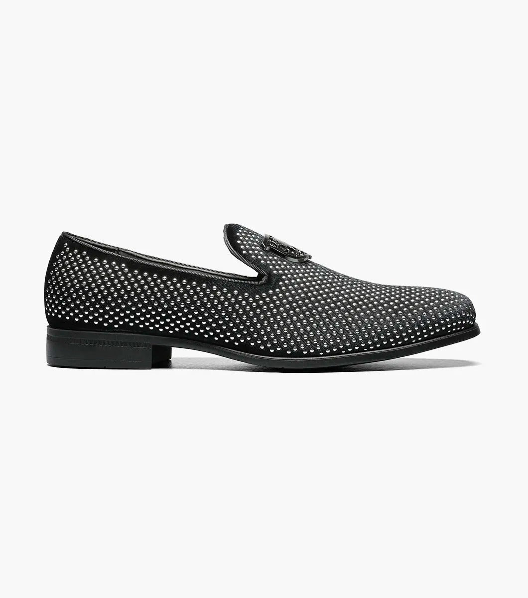 The STACY ADAMS SWAGGER Studded Slip On in black and silver, model 25228-042, is a loafer featuring striking silver studs and the Stacy Adams crest on the upper, exuding a sense of understated elegance.
