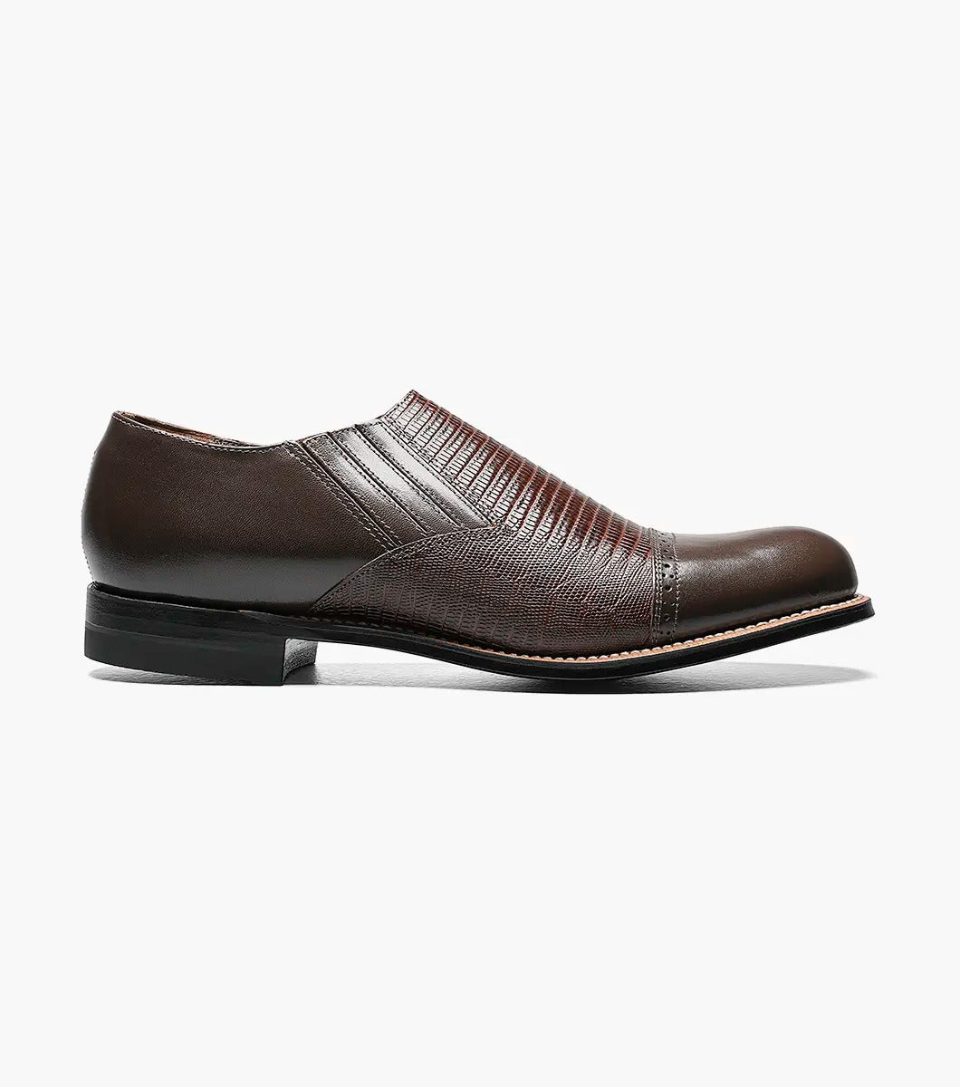 The Stacy Adams - MADISON Cap Toe Slip On in brown is shown in a side profile view against a white background. This shoe features embossed detailing and a low heel, crafted with Goodyear welt construction.