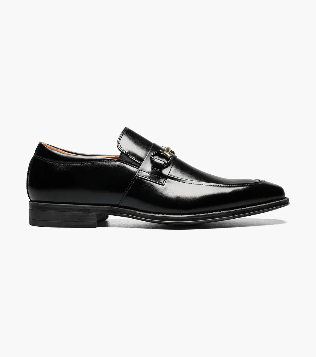 The Stacy Adams PIERCE Moc Toe Bit Slip On in black, style number 25245-001, features a metallic buckle detail and a low heel. It comes with a comfortable Memory Foam insole and is displayed against a white background.