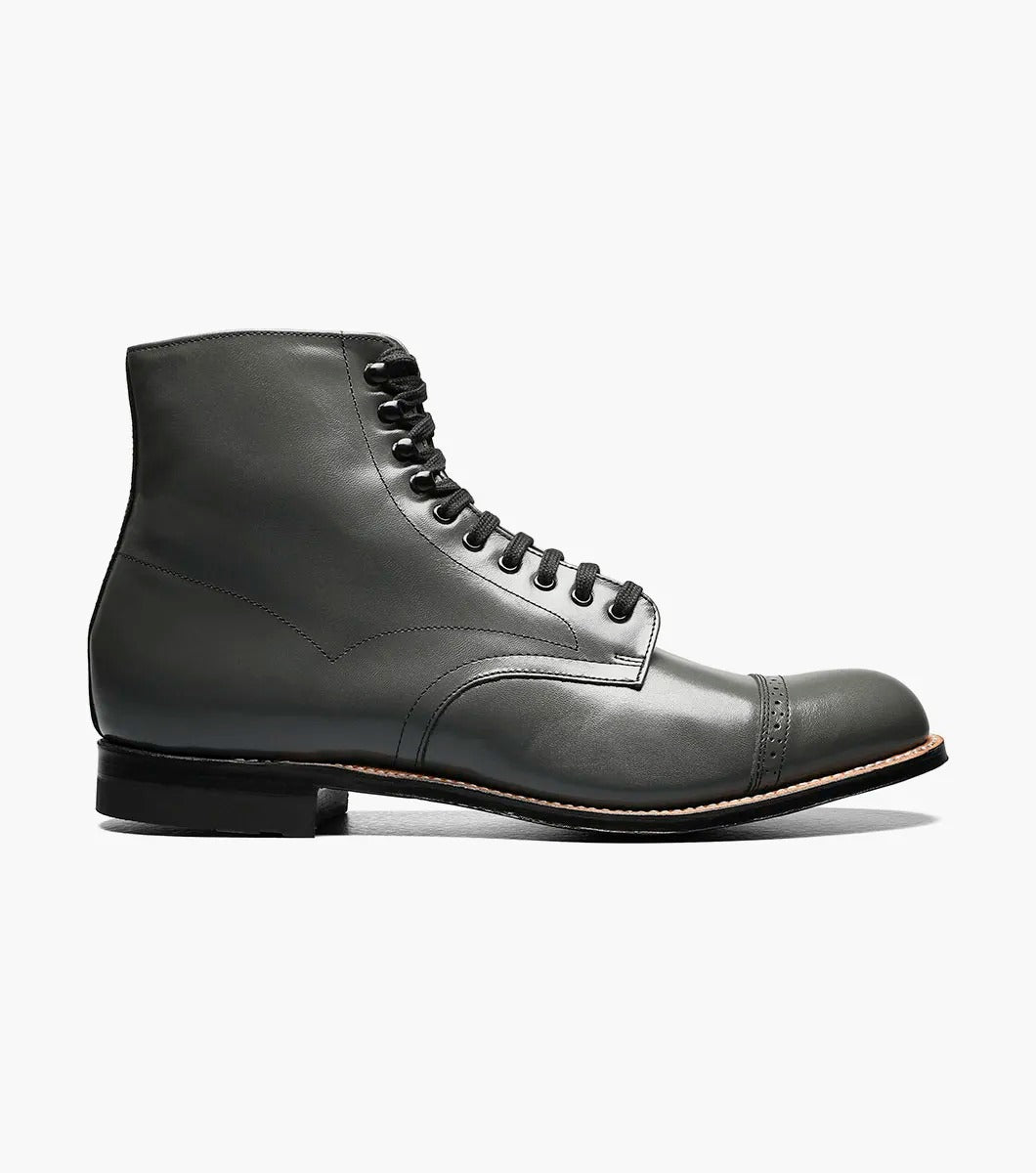 The Stacy Adams MADISON Cap Toe Boot in Steel Gray, made from high-quality kidskin leather, showcases a sophisticated lace-up design and a polished cap toe, enhanced by a sturdy black sole set against a crisp white backdrop.