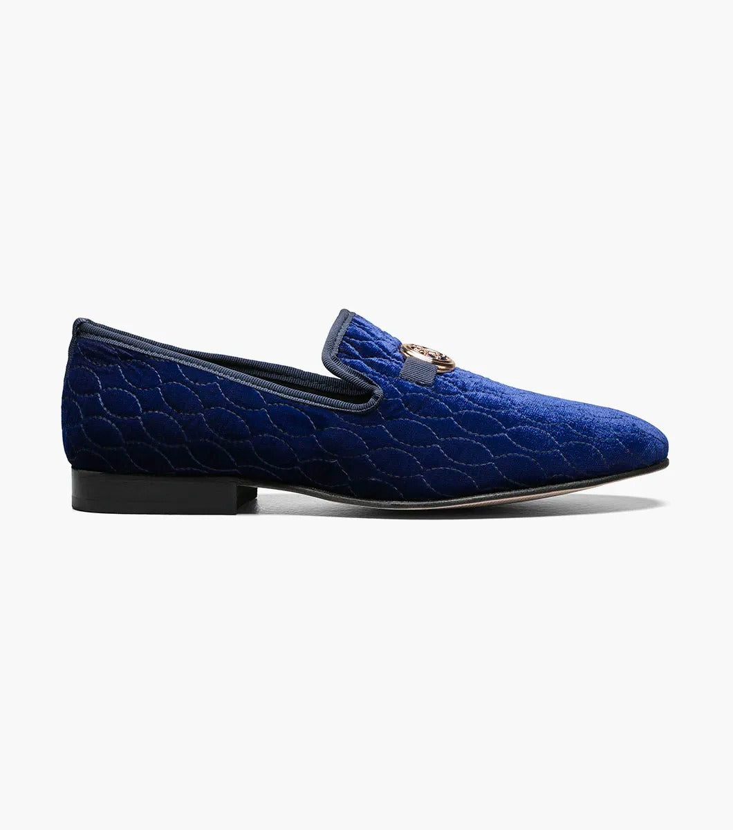 The Stacy Adams VALET Slip On Bit Loafer, model 25166-400, combines quilted velour in a striking blue with a sleek black sole and is elegantly decorated with a gold emblem on top. It also features a Memory Foam insole for enhanced comfort.