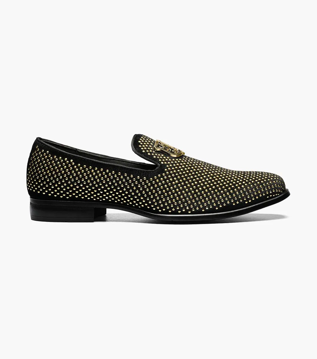 The Stacy Adams - SWAGGER Studded Slip On - Black and Gold - 25228-715 is a black loafer adorned with gold studs and a decorative emblem on top, featuring a comfortable memory foam insole.