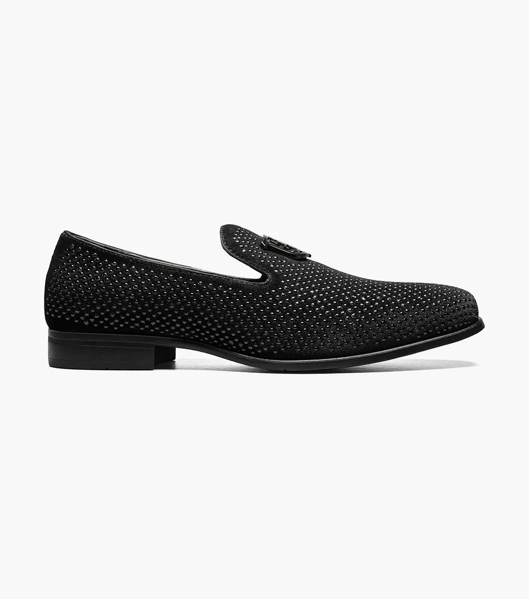 The Stacy Adams - SWAGGER Studded Slip On in black (style 25228-001) features a striking silver emblem, accompanied by a textured design and low heel. These shoes offer a sophisticated touch with the added comfort of memory foam, making them ideal for any occasion.