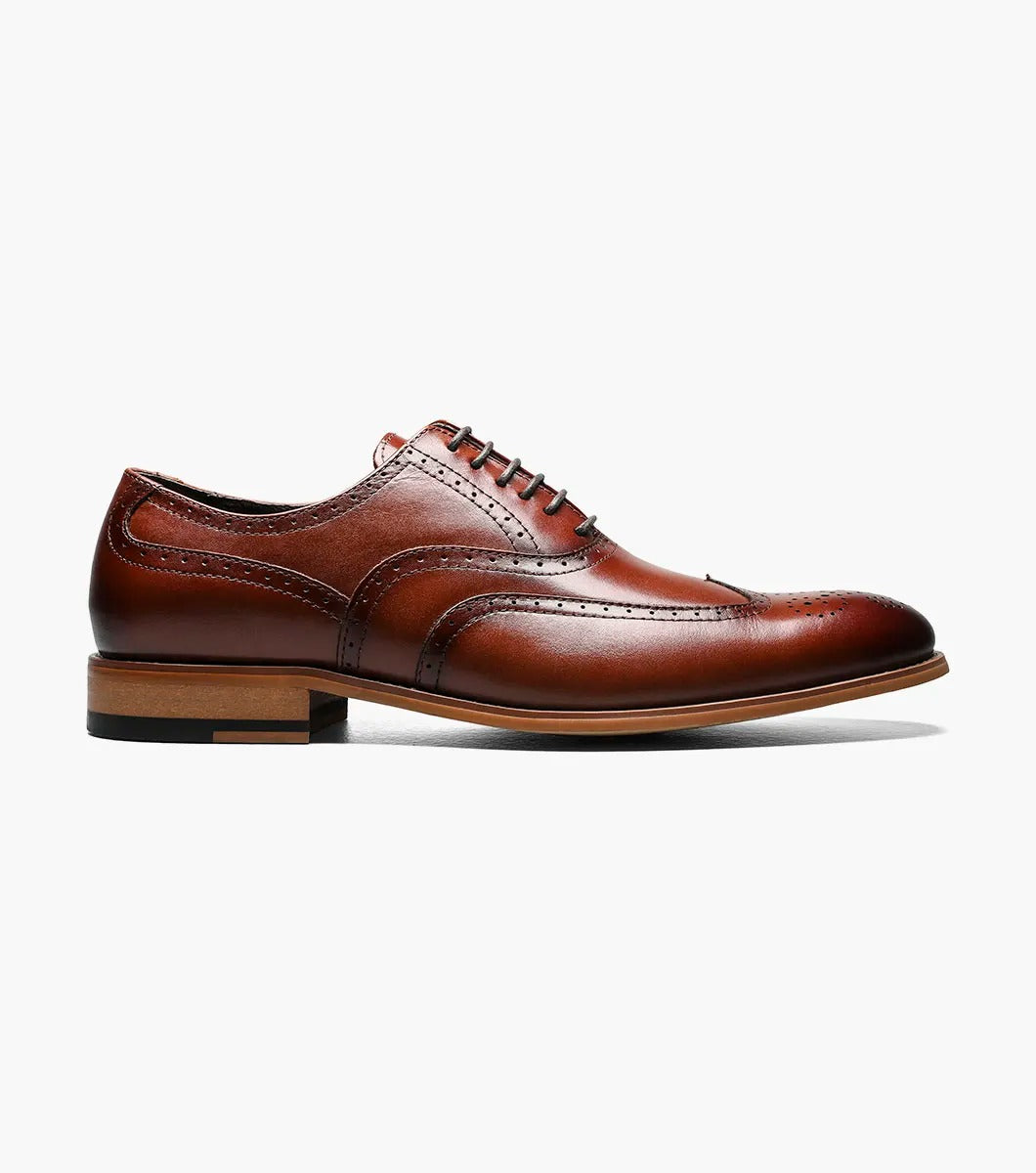 The Stacy Adams DUNBAR Wingtip Oxford shoe, model number 25064-221 in Cognac, showcases a leather upper with intricate stitching and perforations. This elegant design is completed with a low wooden heel, creating timeless sophistication against a white background.