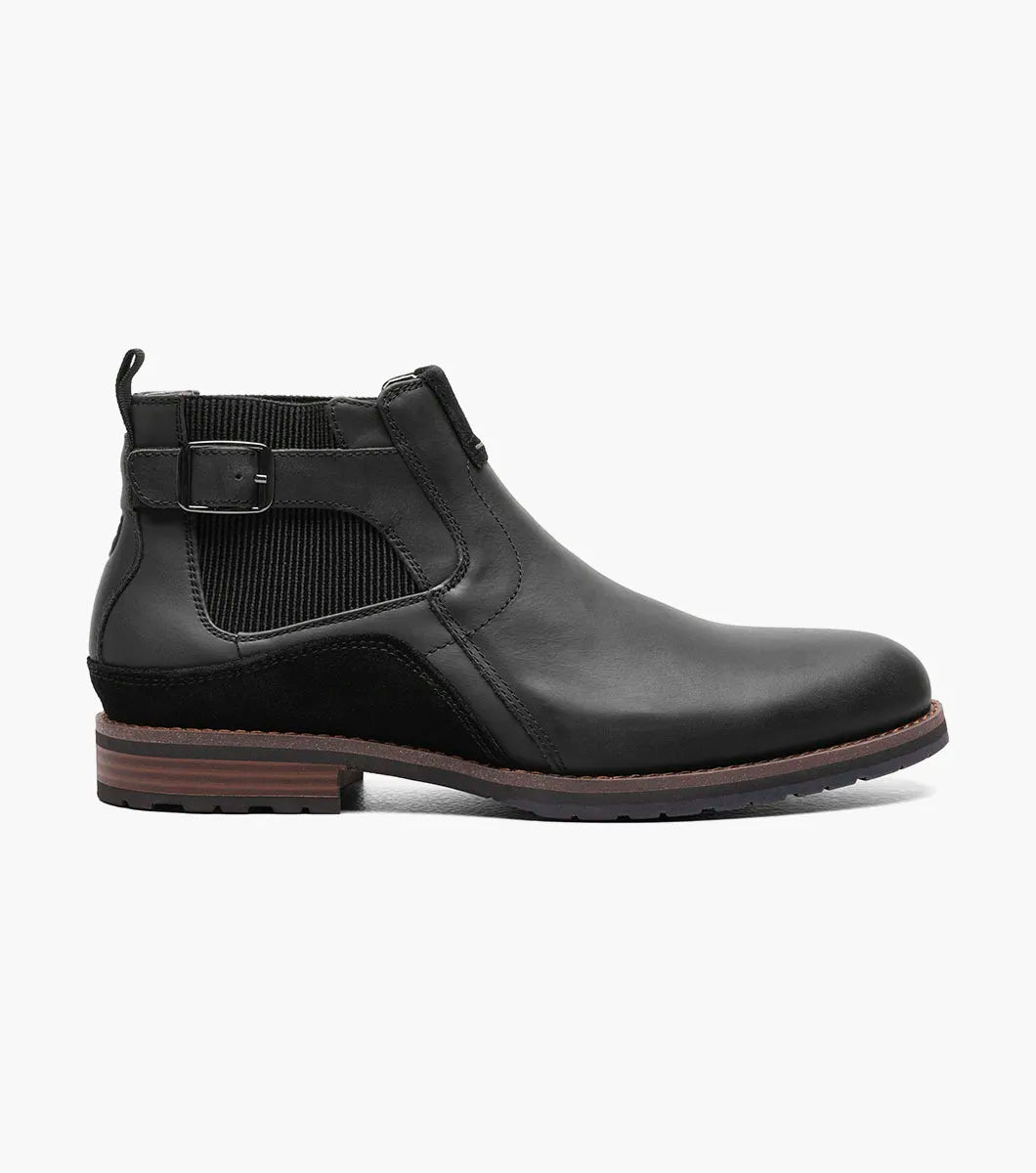 The Stacy Adams OSKAR Plain Toe Chelsea Boot in Black Waxy features a black leather design with a side buckle, an elastic gusset, and a brown sole. Its stylish mixed material upper adds an extra touch of flair.