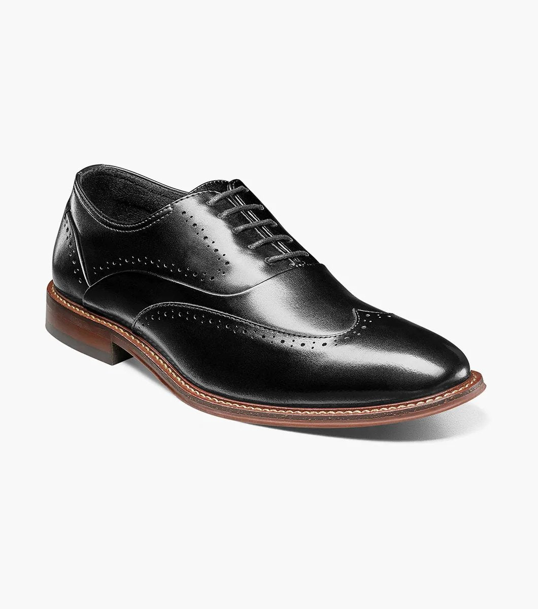 Introducing the Stacy Adams MACARTHUR Wingtip Oxford in Black Smooth (model 25489-005), a dress shoe crafted from burnished leather, featuring elegant decorative perforations and lace-up design, complete with a distinctive brown sole.