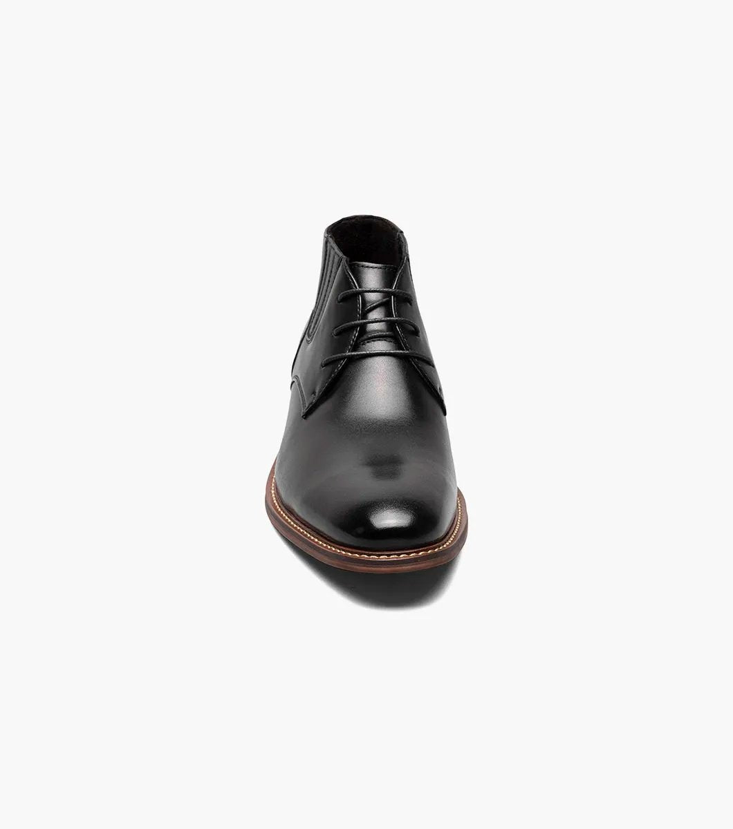 Introducing the Stacy Adams - MAXWELL Plain Toe Chukka Boot in Black, model 25551-001. This versatile boot features a sleek polished finish, a contrasting brown welt, and three pairs of lace eyelets. Set atop a wooden sole, it is designed with anatomical arch support to ensure maximum comfort.