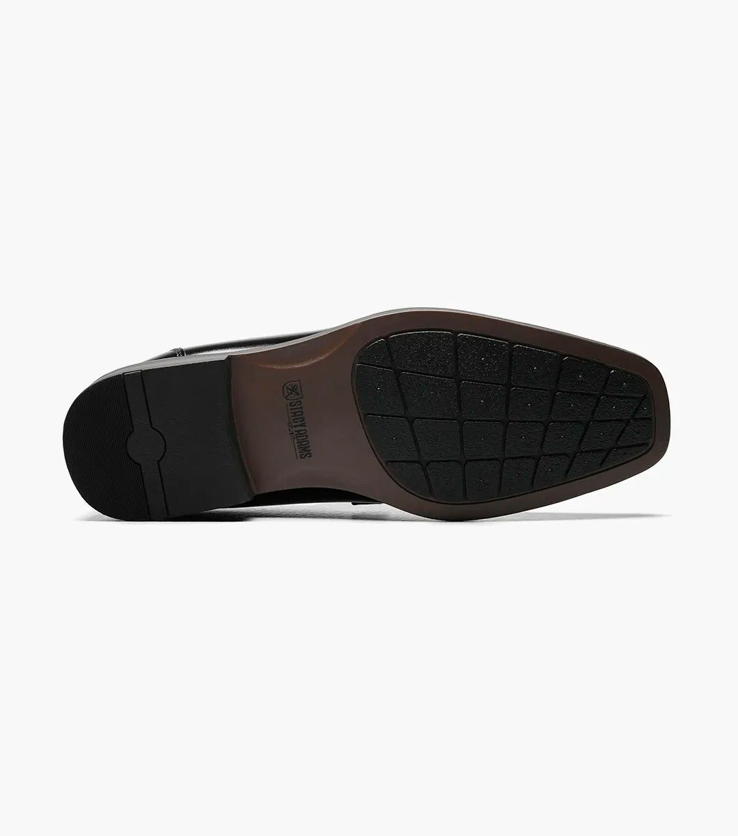 The Stacy Adams CADE Bike Toe Slip On in black, model 20126-001, is a stylish black leather loafer with a slip-on design. It features a gunmetal bit and a low heel, set against a plain white background.