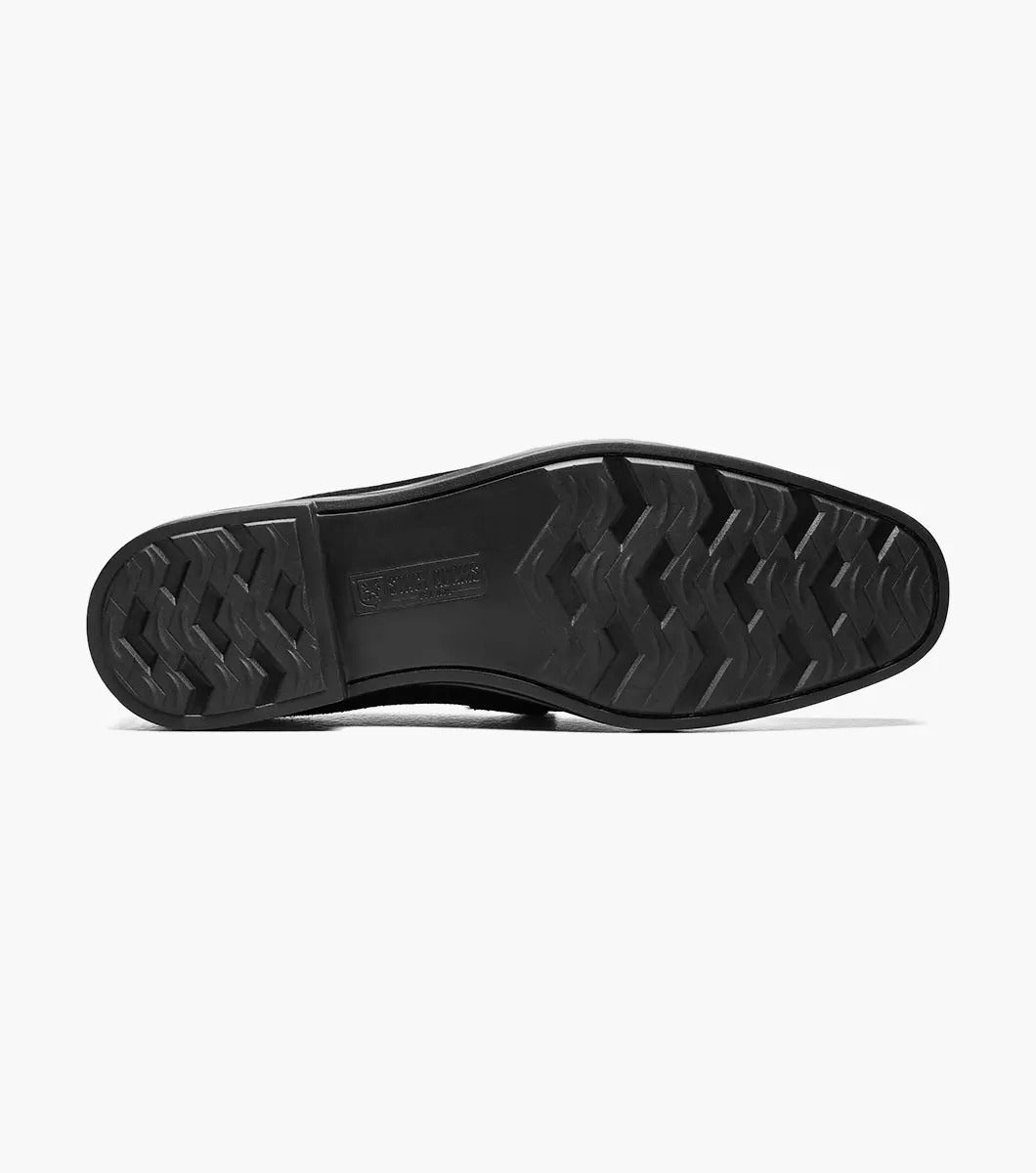 The Stacy Adams NEVILLE Moc Toe Bit Slip On in black suede showcases a metal chain detail on top, accompanied by a slightly elevated heel and stitched accents. Its cushioned insole provides comfort for all-day wear.