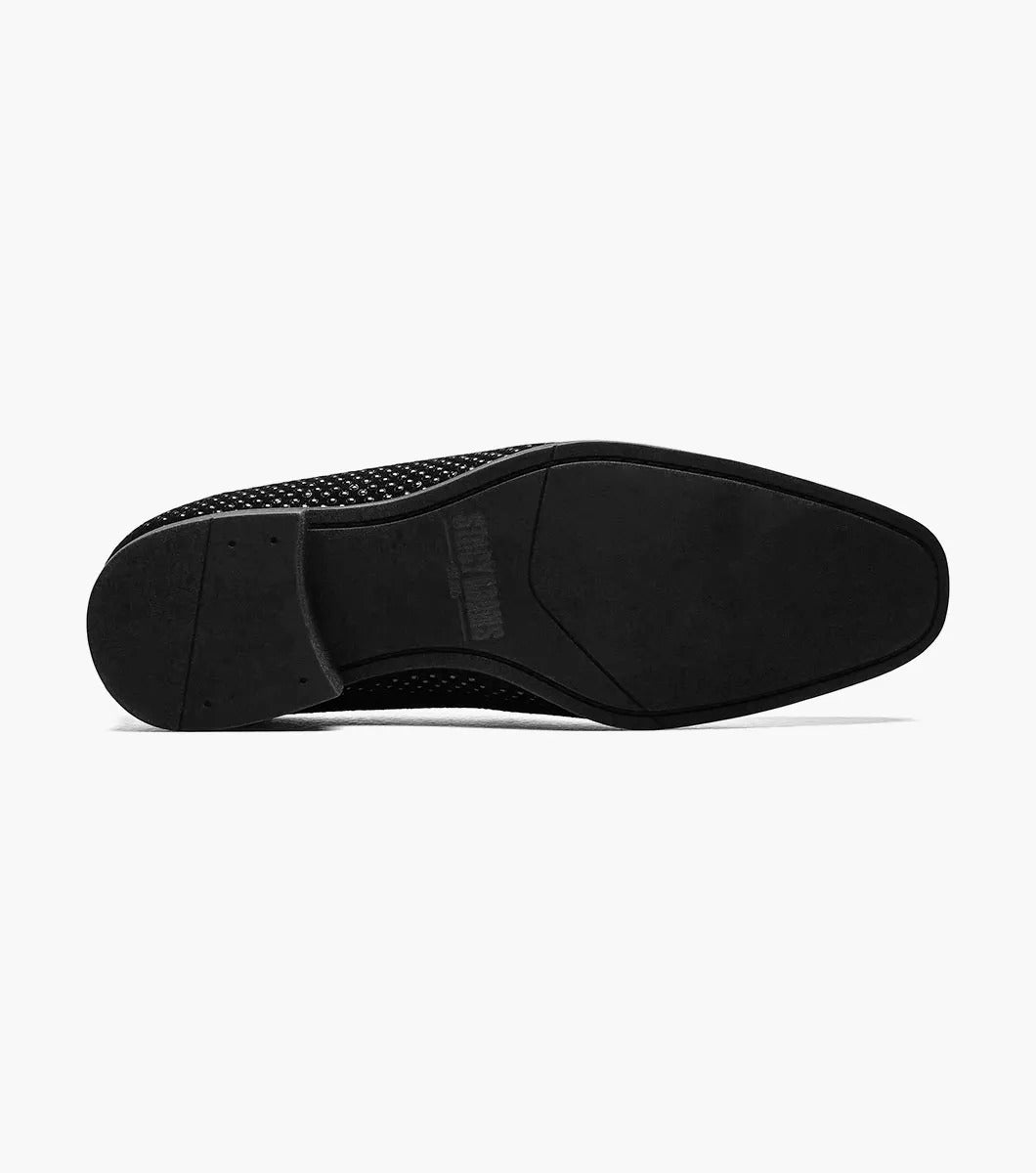 The Stacy Adams - SWAGGER Studded Slip On in black (style 25228-001) features a striking silver emblem, accompanied by a textured design and low heel. These shoes offer a sophisticated touch with the added comfort of memory foam, making them ideal for any occasion.