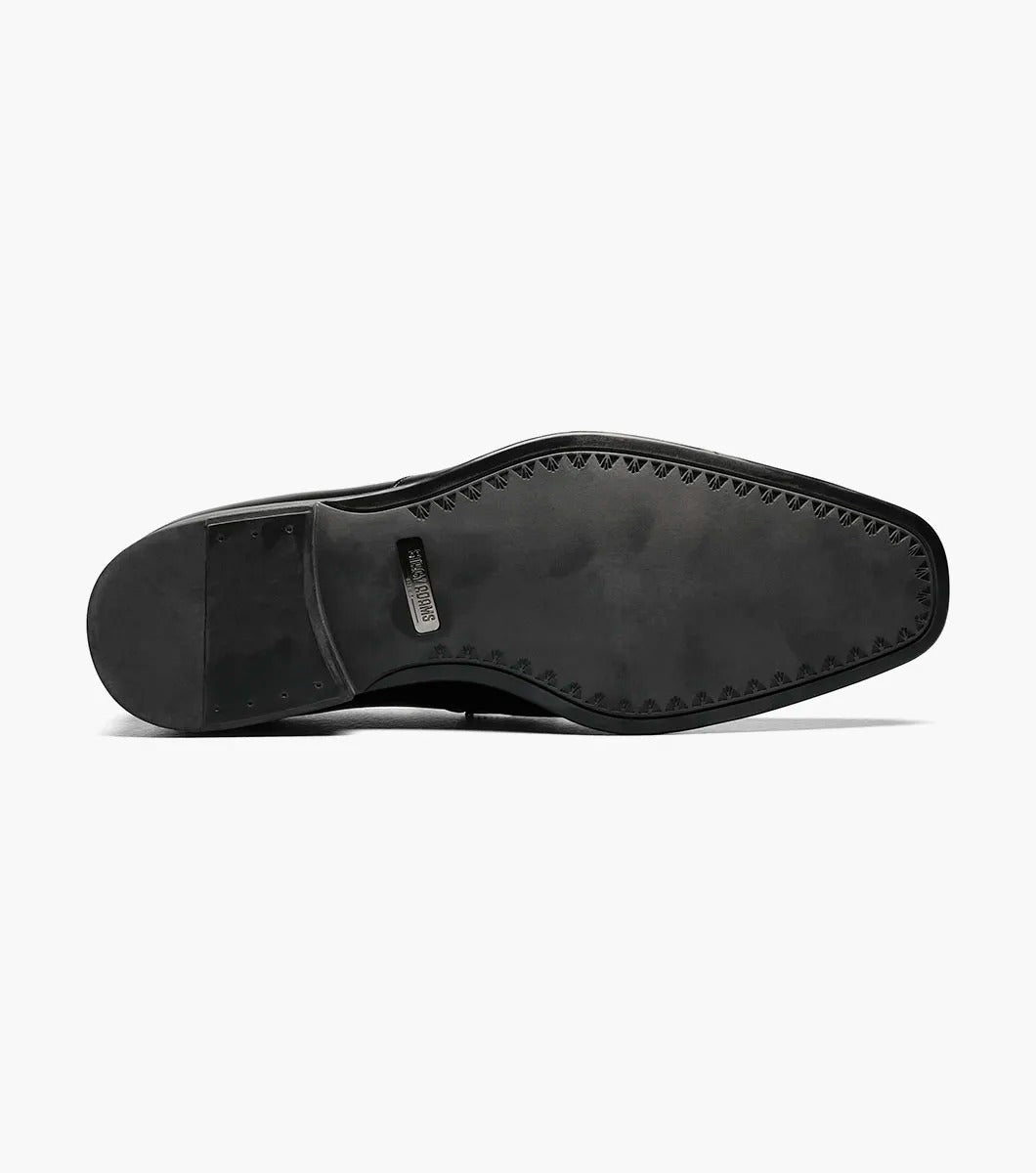 The Stacy Adams PIERCE Moc Toe Bit Slip On in black, style number 25245-001, features a metallic buckle detail and a low heel. It comes with a comfortable Memory Foam insole and is displayed against a white background.