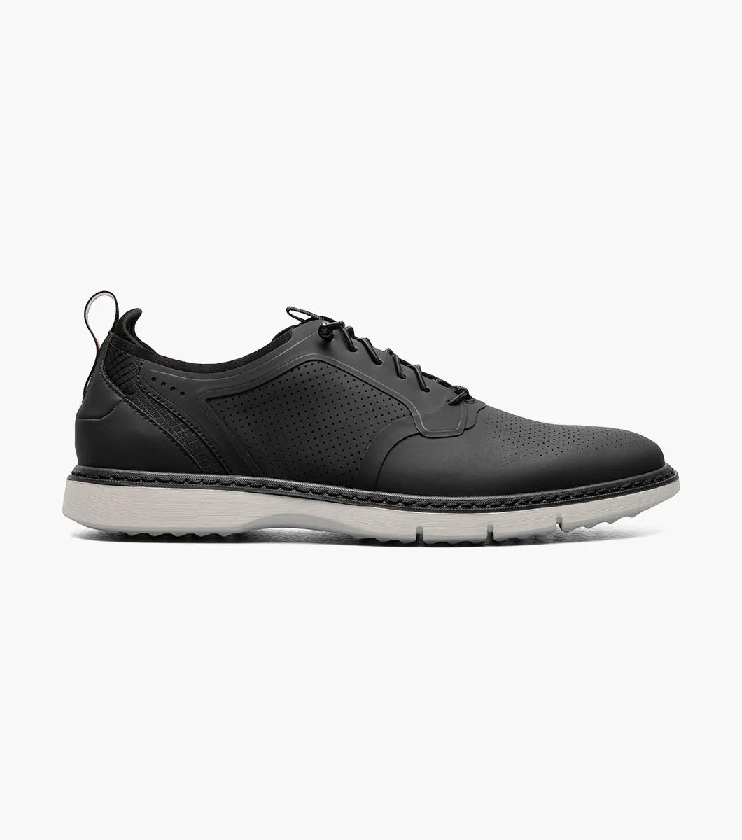 The Stacy Adams SYNCHRO Plain Toe Elastic Lace Up shoe in black (style 25518-001) is a casual dress shoe featuring an elastic lace-up design with a perforated pattern and white sole, complemented by the comfortable RedZone footbed. It is showcased from the side against a simple backdrop.