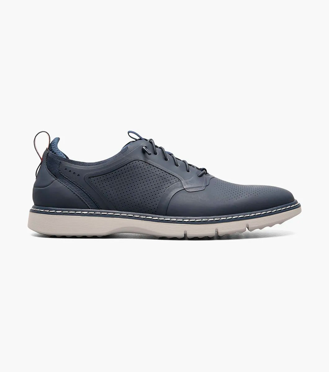 The Stacy Adams SYNCHRO Plain Toe Elastic Lace Up shoe in navy boasts a perforated pattern and a red pull tab, complemented by a light gray sole. It is designed with the RedZone removable footbed to provide anatomical arch support.