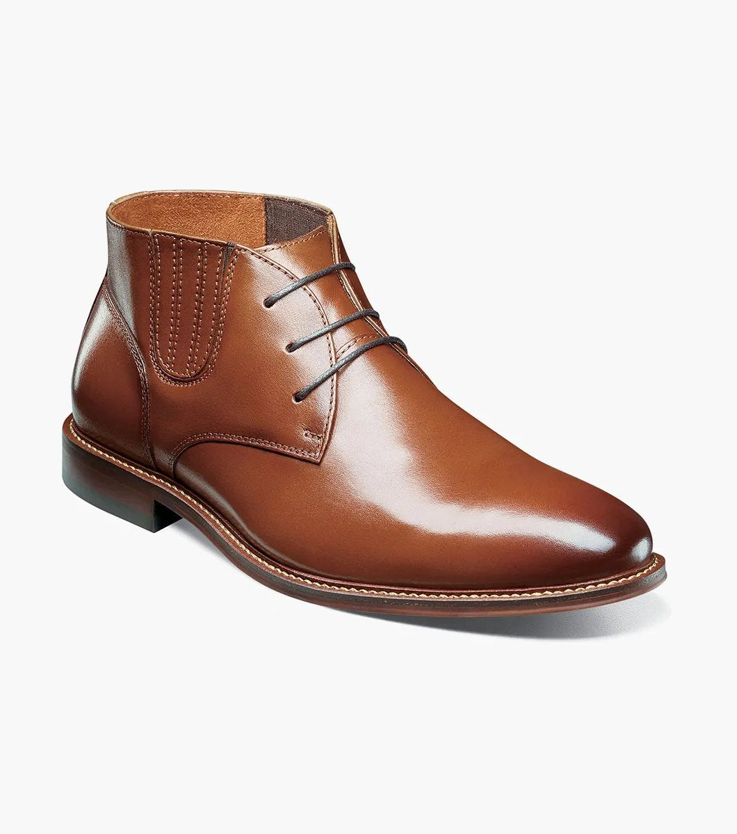 The Stacy Adams Maxwell Plain Toe Chukka Boot in Cognac features a sophisticated leather design with three eyelets, detailed stitching, and a versatile low heel, making it ideal for both dressy and casual events.