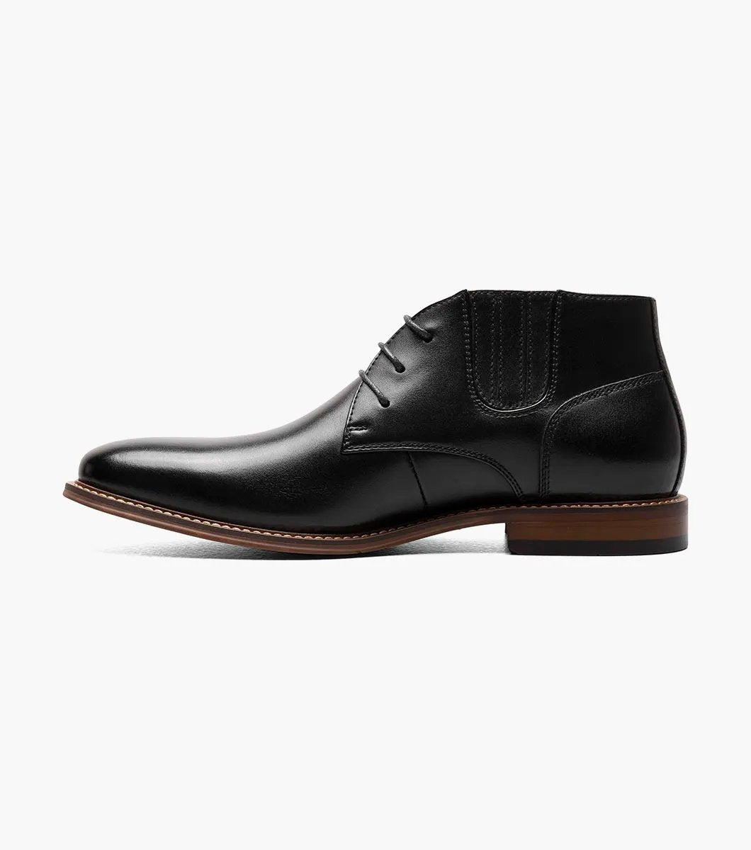 Introducing the Stacy Adams - MAXWELL Plain Toe Chukka Boot in Black, model 25551-001. This versatile boot features a sleek polished finish, a contrasting brown welt, and three pairs of lace eyelets. Set atop a wooden sole, it is designed with anatomical arch support to ensure maximum comfort.