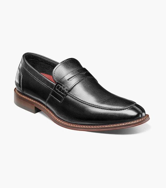 The Stacy Adams MARLOWE Algonquin Moc Toe Penny Slip On in black, featuring a refined leather upper and a contrasting brown sole, is displayed against a plain background.